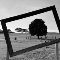 Tilted empty frame overlooking people walking across a grassy field