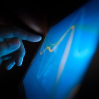 Hand interacting with a blue screen showing an abstract line graphic